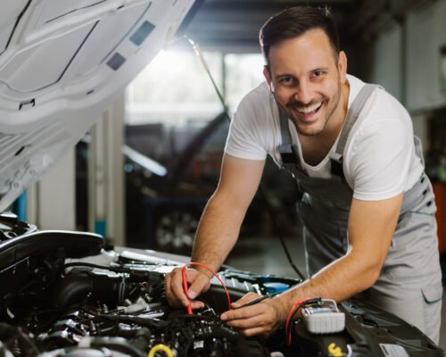Happy mechanic working on car diagnostic in a repair shop. He is looking at camera